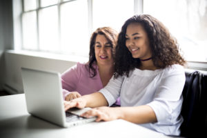 Carer And Teenage Daughter Looking At Laptop Together